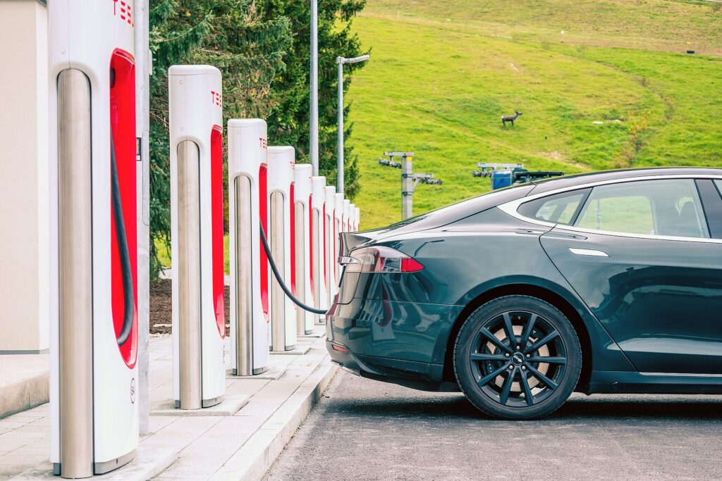 Black Tesla pluged in at one of a row of Tesla Superchargers